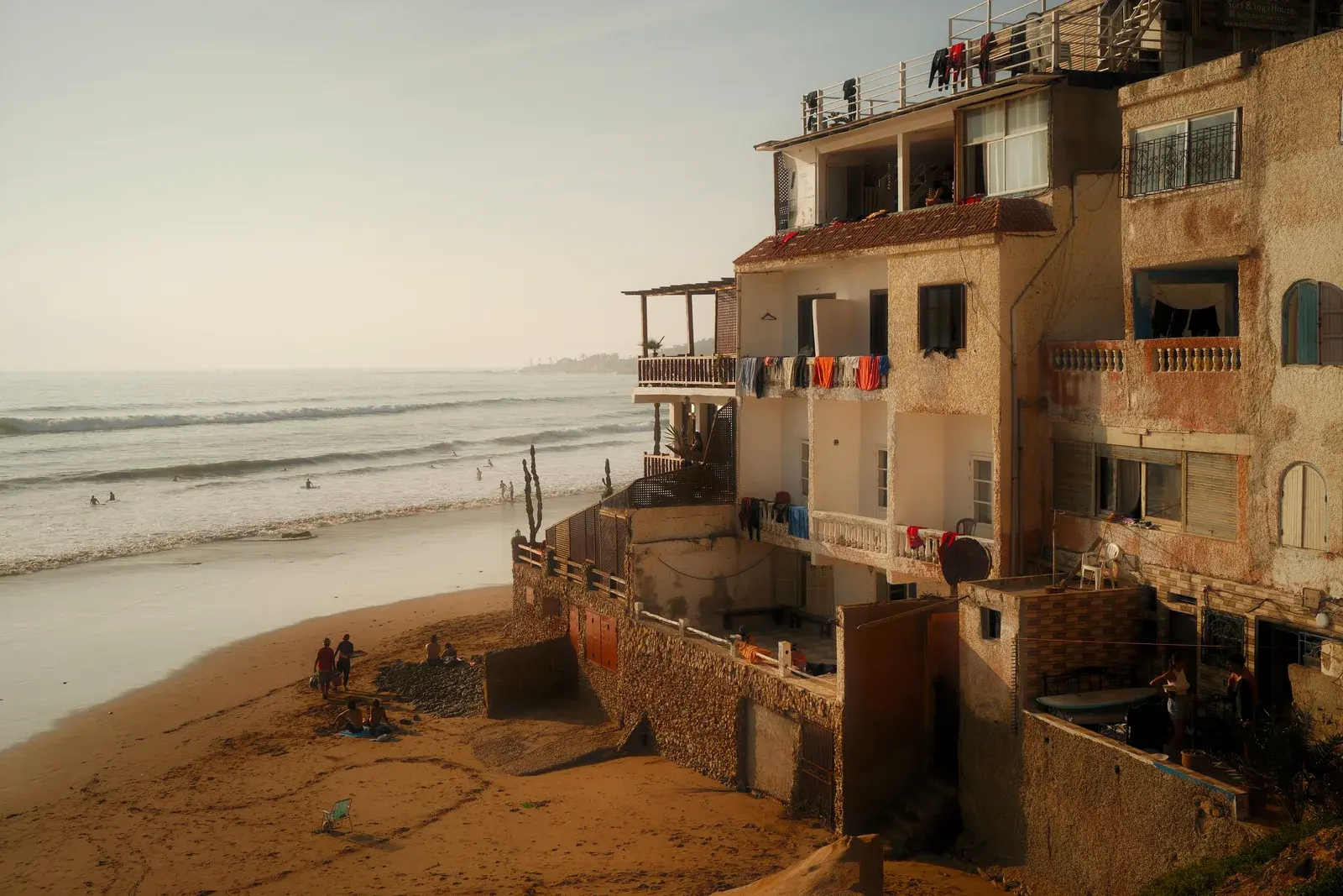 Die Häuser von Taghazout in Marokko stehen direkt am Strand, Surfer in den Wellen im Abendlicht