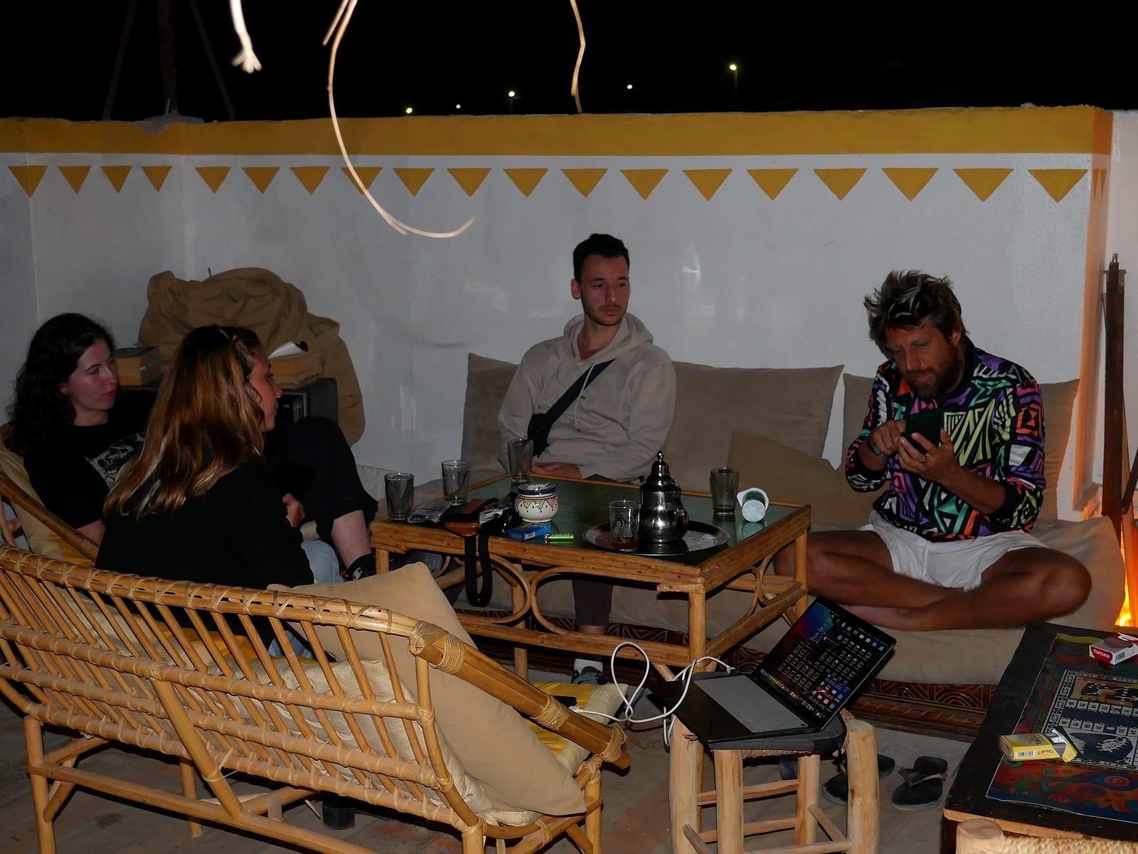 Guests sitting with mint tea on the rooftop lounge of a surf hostel in Tamraght, Morocco, in the evening
