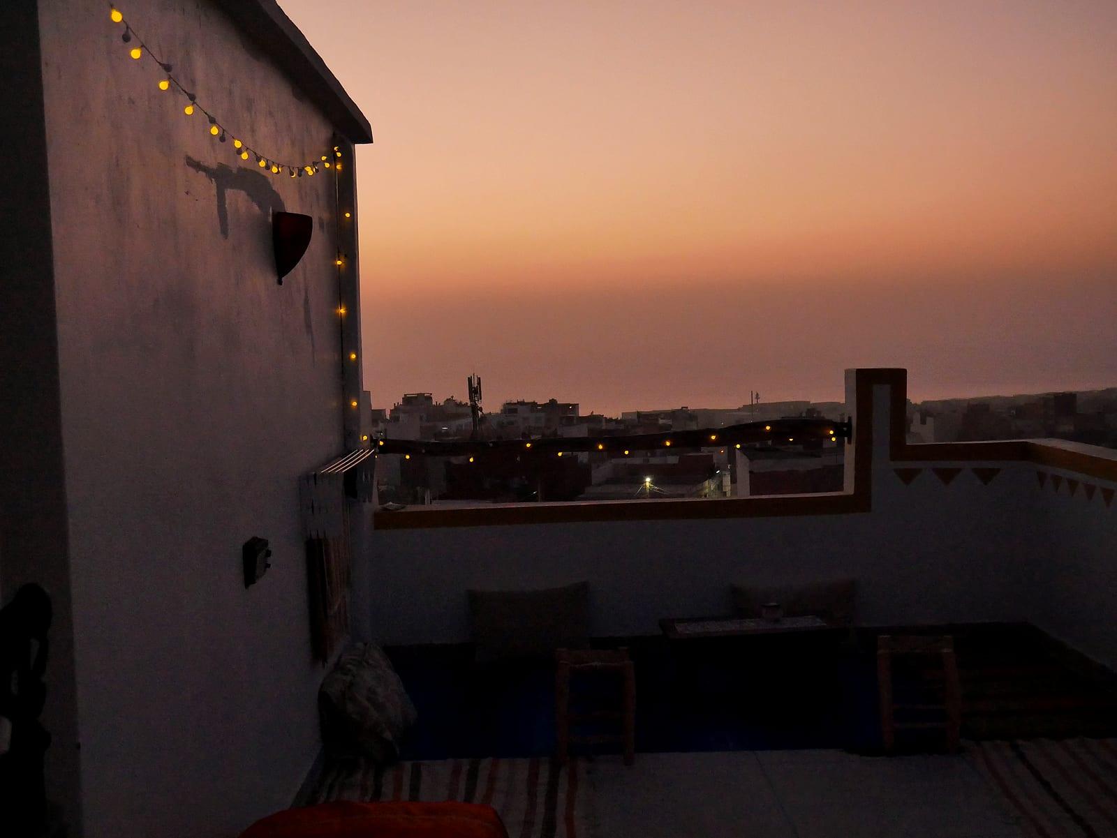 Sonnenuntergang vom Rooftop eines Surfcamps in Tamraght, Marokko, mit Lichterkette und Atlantik am Horizont