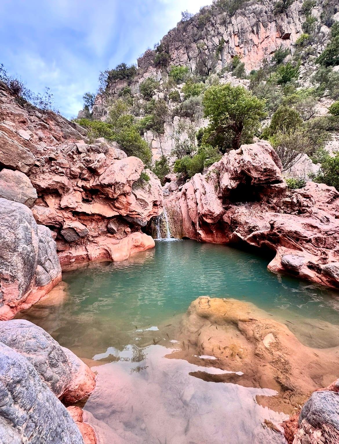 Ein türkisfarbener Naturpool mit kleinem Wasserfall zwischen roten Felsen im Paradise Valley, Marokko