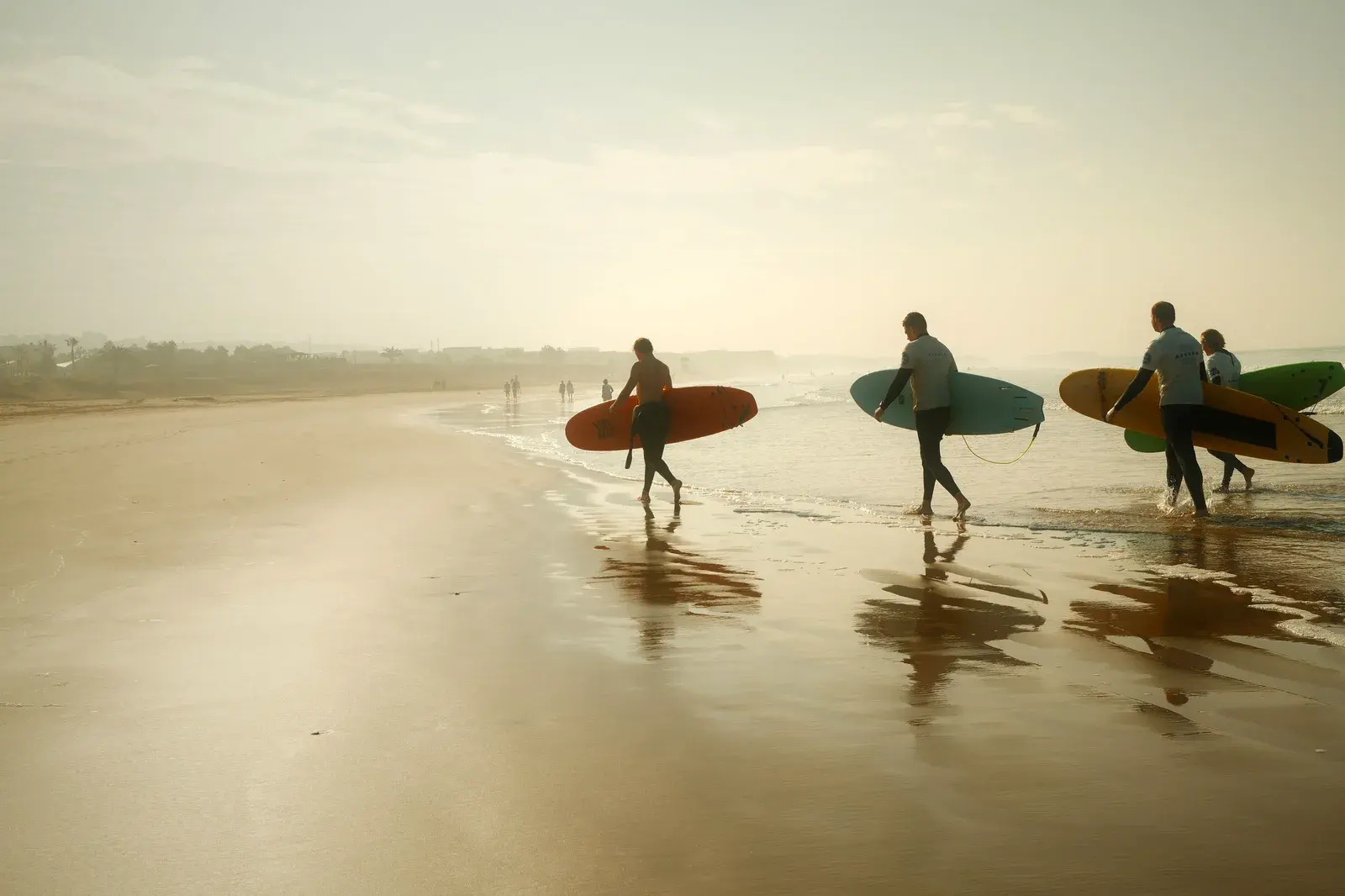 Surfer laufen bei Sonnenuntergang mit ihren Boards Richtung Atlantik an einem marokkanischen Strand